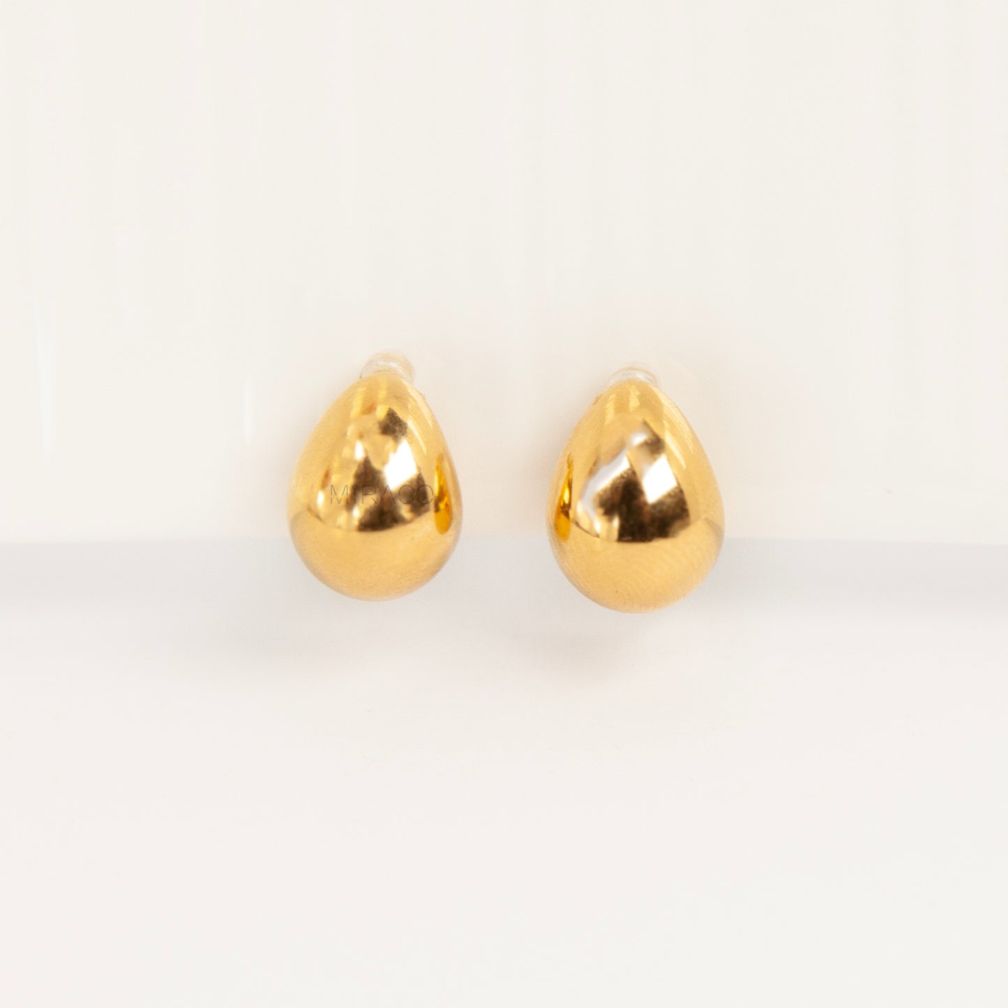 Pair of polished gold teardrop-shaped clip-on earrings with clear invisible resin backs.