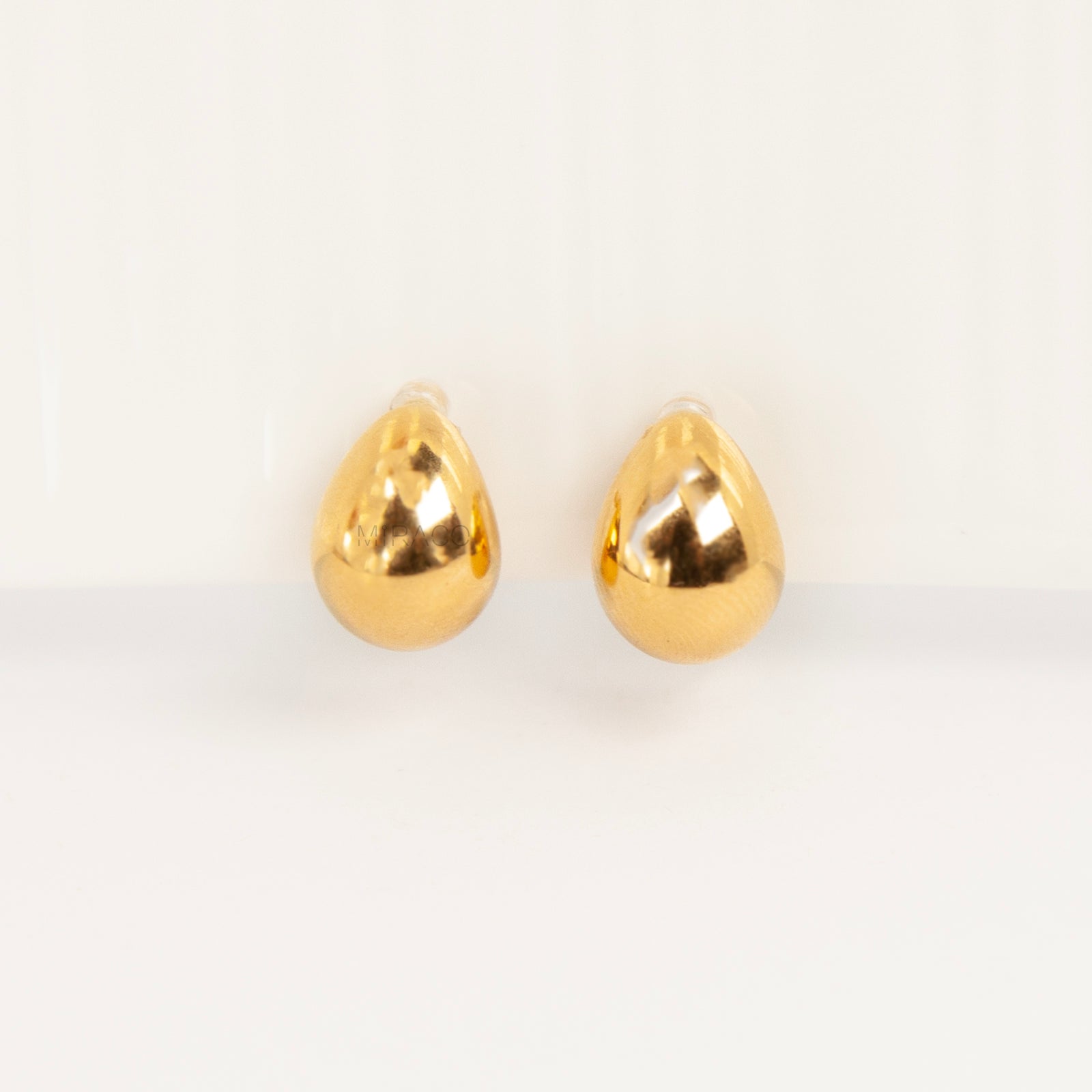 Pair of polished gold teardrop-shaped clip-on earrings with clear invisible resin backs.