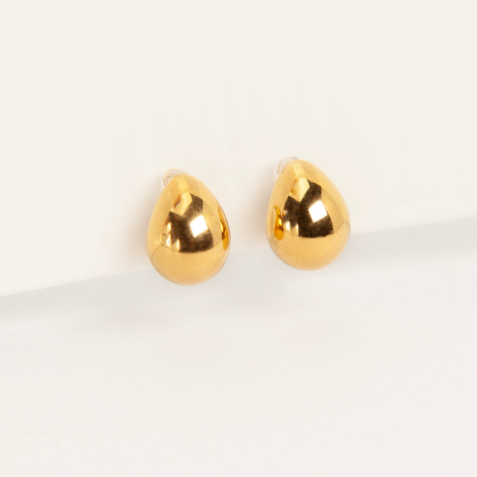 Pair of polished gold teardrop-shaped clip-on earrings with clear invisible resin backs.