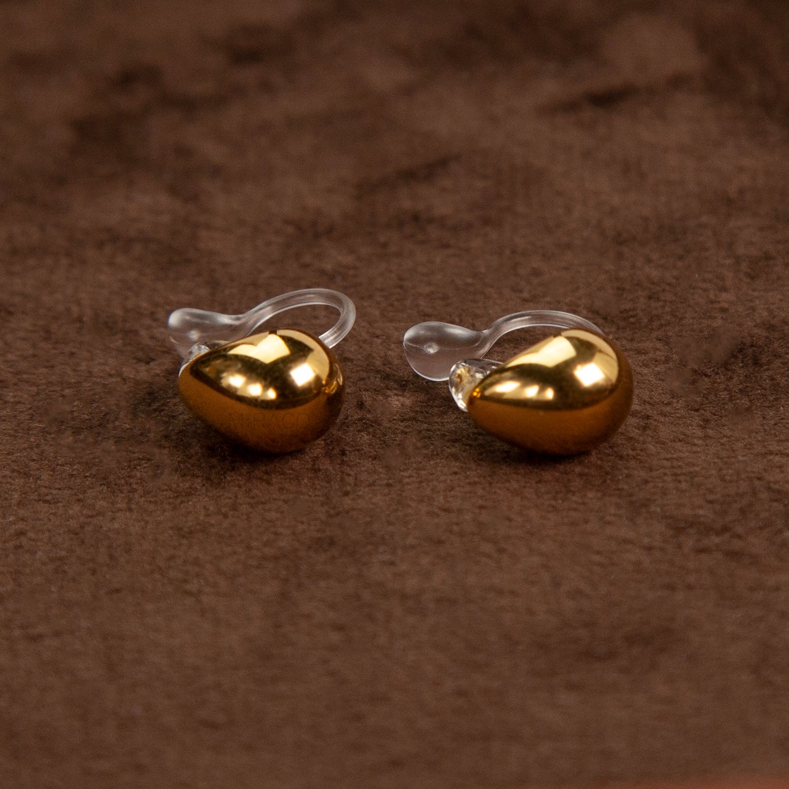 Pair of polished gold teardrop-shaped clip-on earrings with clear invisible resin backs.