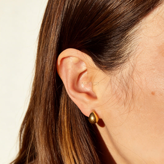 Pair of polished gold teardrop-shaped clip-on earrings with clear invisible resin backs.