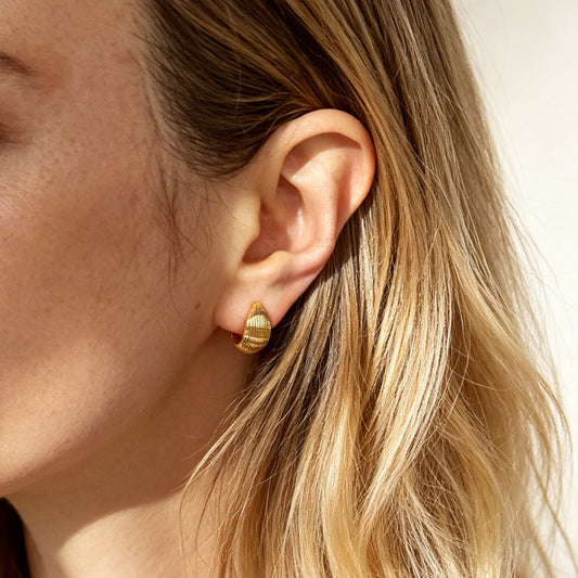 A pair of chunky, polished gold-tone dome clip-on earrings featuring a textured ribbed pattern and adjustable gold screw-back fasteners for non-pierced ears.