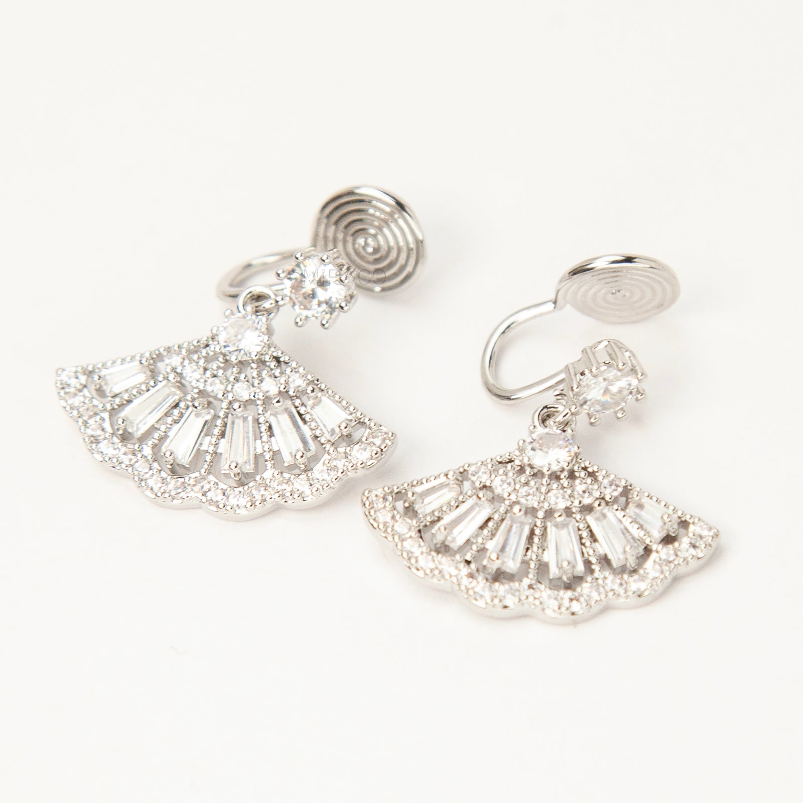 A pair of silver-tone Art Deco style clip-on drop earrings featuring a fan-shaped design set with baguette and round clear crystals, with adjustable coil-spring backs.