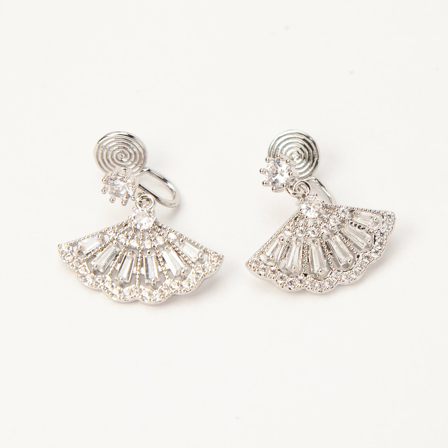 A pair of silver-tone Art Deco style clip-on drop earrings featuring a fan-shaped design set with baguette and round clear crystals, with adjustable coil-spring backs.