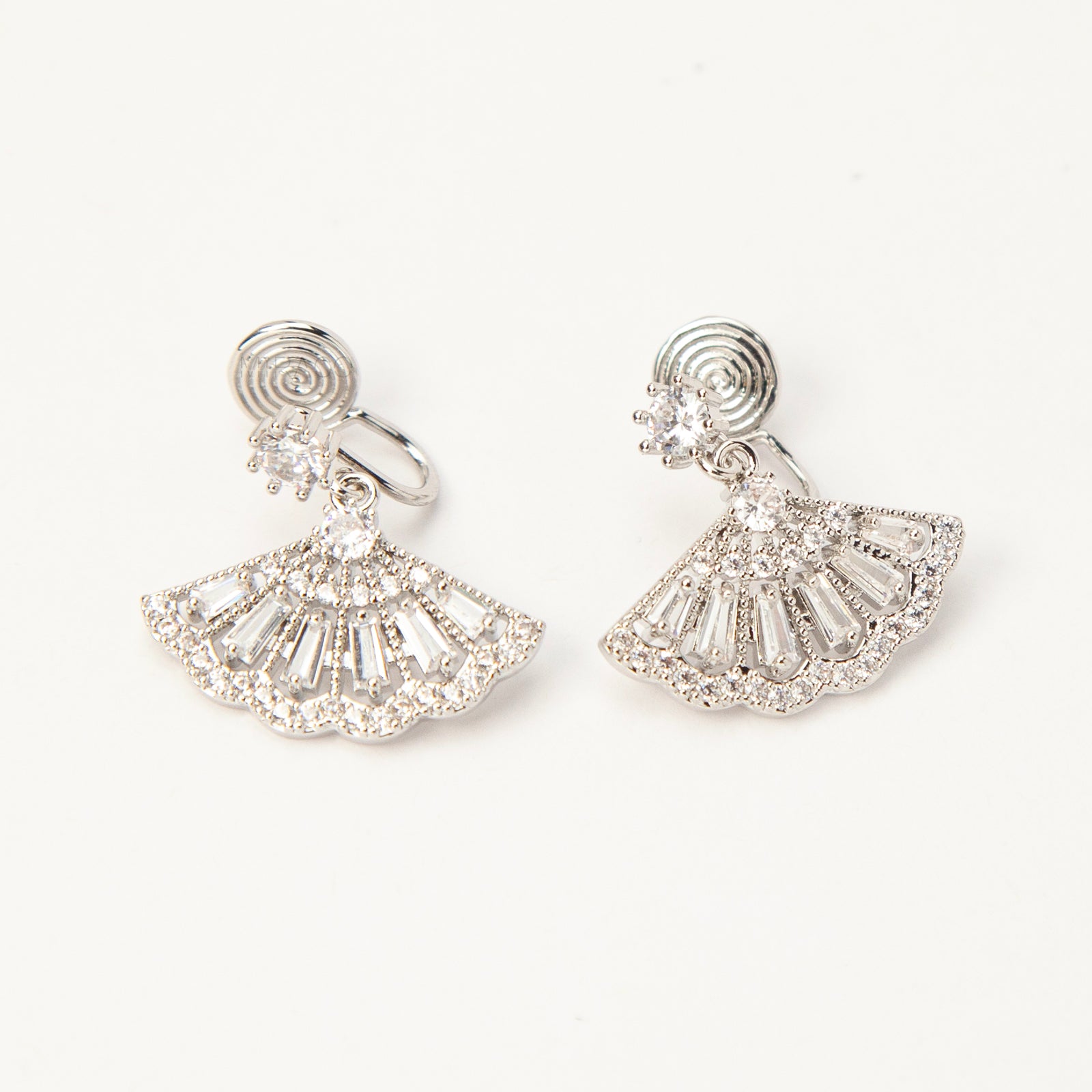 A pair of silver-tone Art Deco style clip-on drop earrings featuring a fan-shaped design set with baguette and round clear crystals, with adjustable coil-spring backs.
