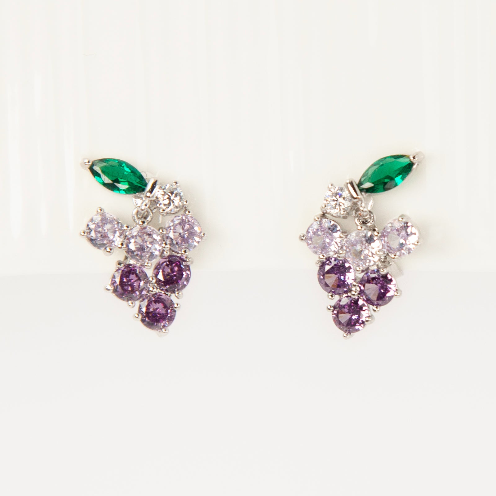 A pair of silver-tone clip-on earrings in the shape of a grape cluster, featuring various shades of round purple crystals and a green marquise-cut crystal leaf