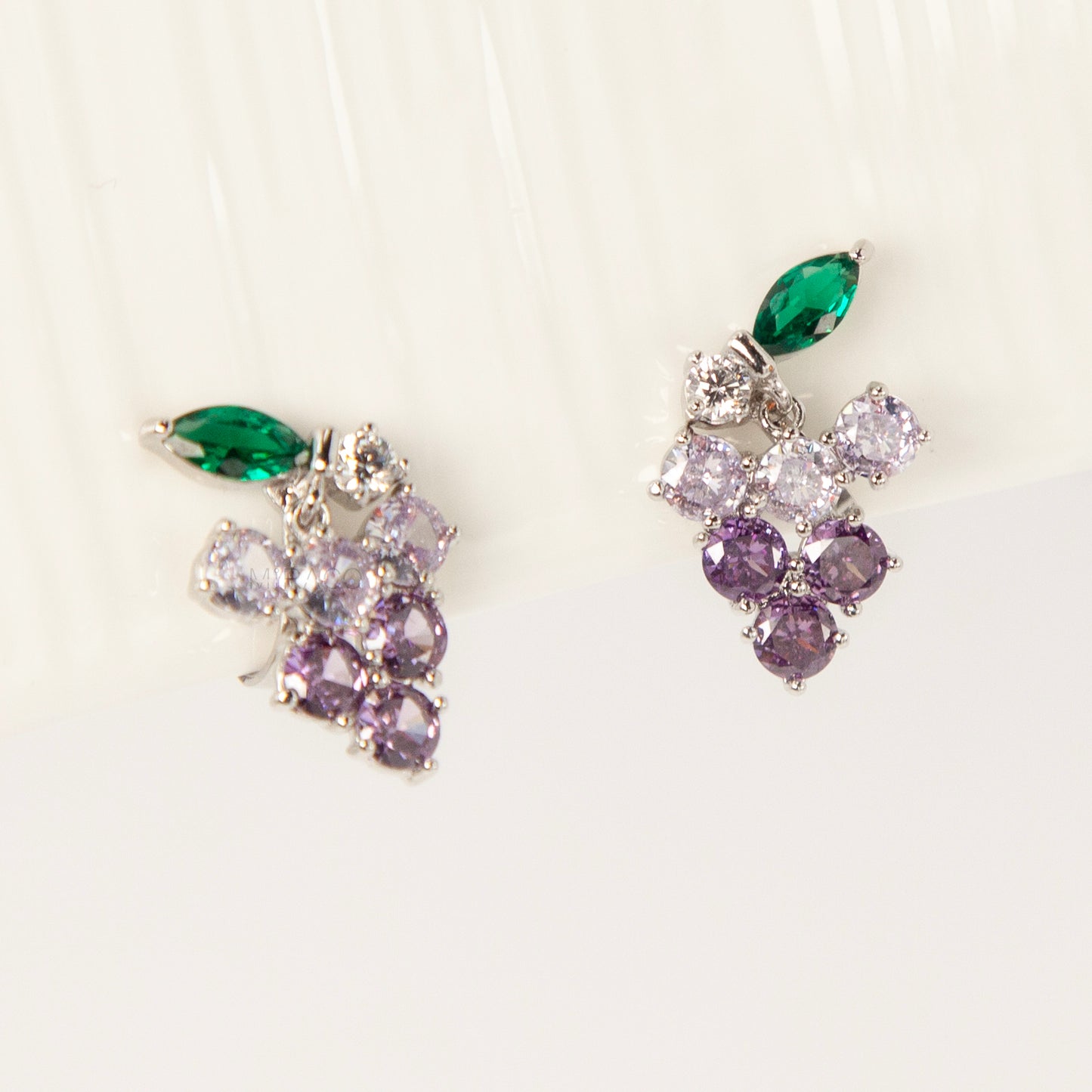 A pair of silver-tone clip-on earrings in the shape of a grape cluster, featuring various shades of round purple crystals and a green marquise-cut crystal leaf