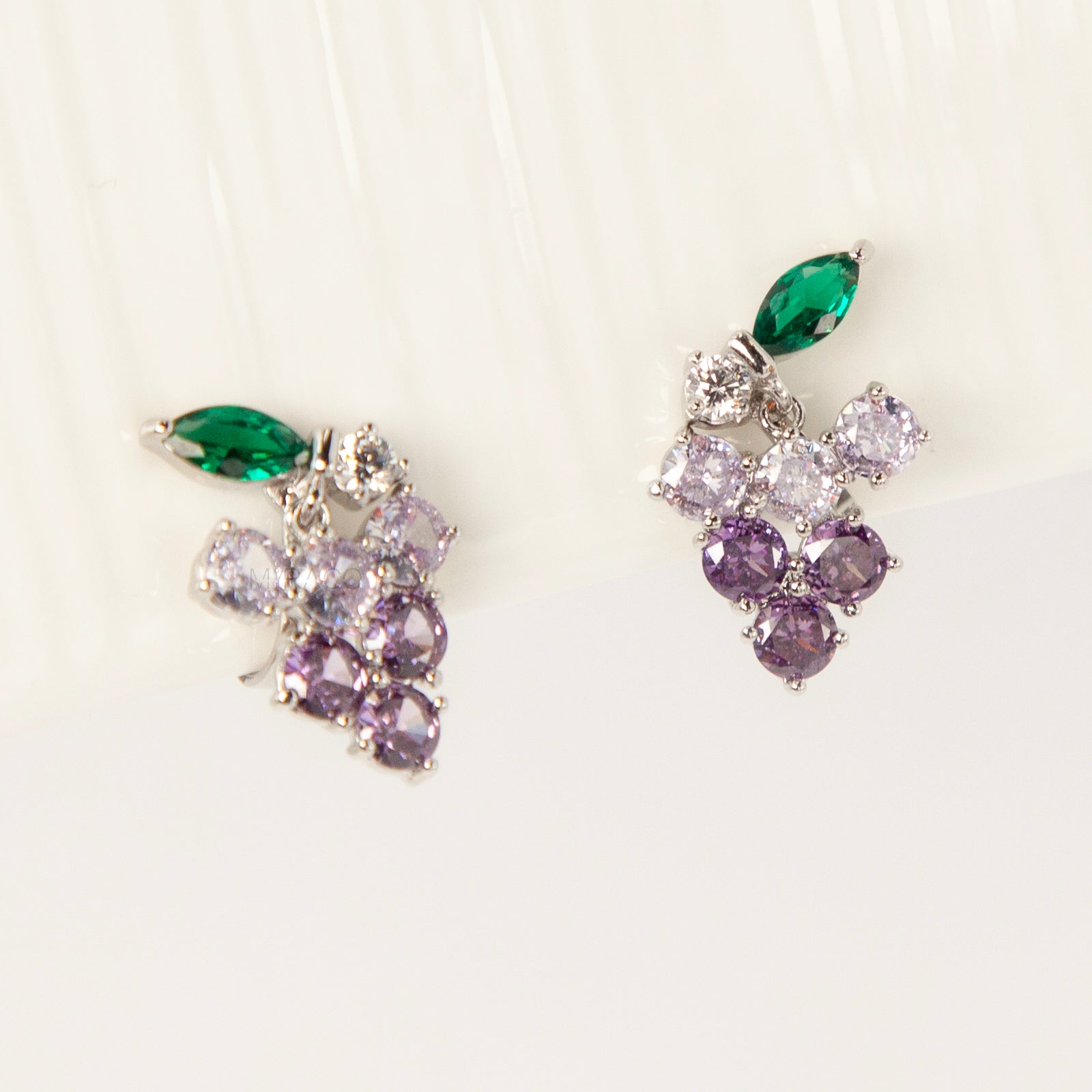 A pair of silver-tone clip-on earrings in the shape of a grape cluster, featuring various shades of round purple crystals and a green marquise-cut crystal leaf