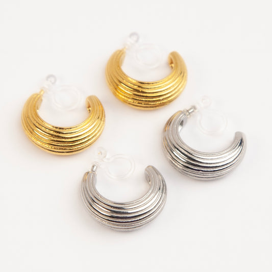 Two pairs of ribbed C-shaped hoop earrings, one in gold and one in silver, featuring clear resin clip-on backs for non-pierced ears
