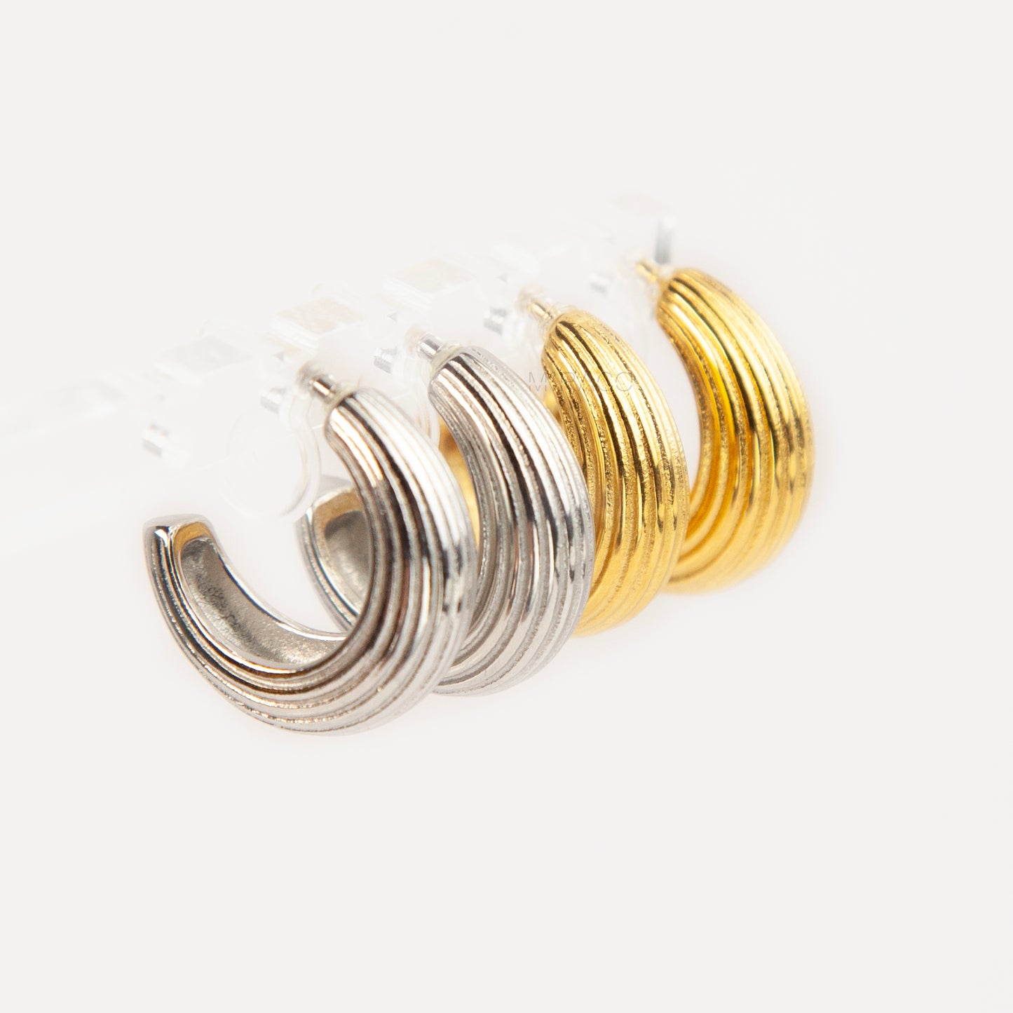 Two pairs of ribbed C-shaped hoop earrings, one in gold and one in silver, featuring clear resin clip-on backs for non-pierced ears