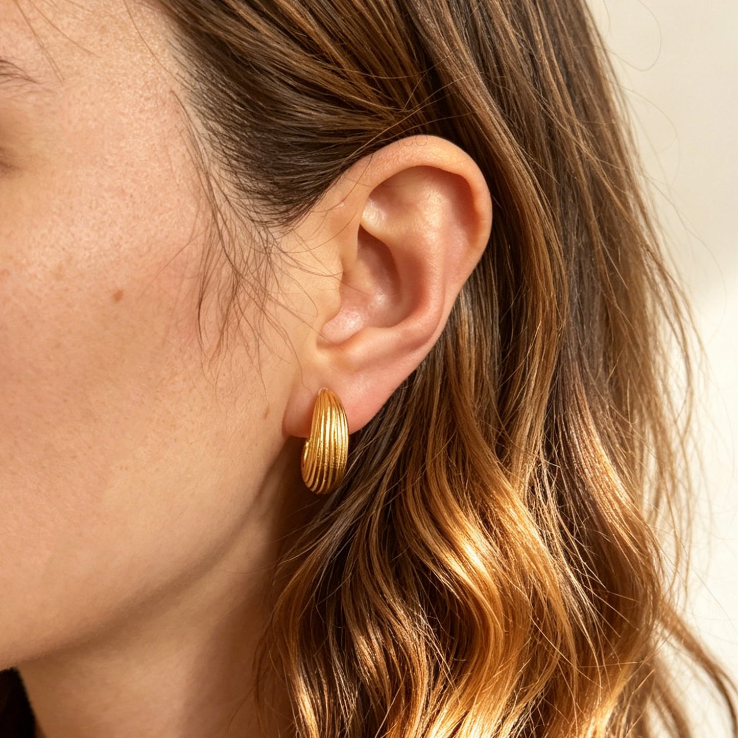 Two pairs of ribbed C-shaped hoop earrings, one in gold and one in silver, featuring clear resin clip-on backs for non-pierced ears
