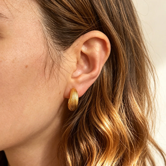 Two pairs of ribbed C-shaped hoop earrings, one in gold and one in silver, featuring clear resin clip-on backs for non-pierced ears