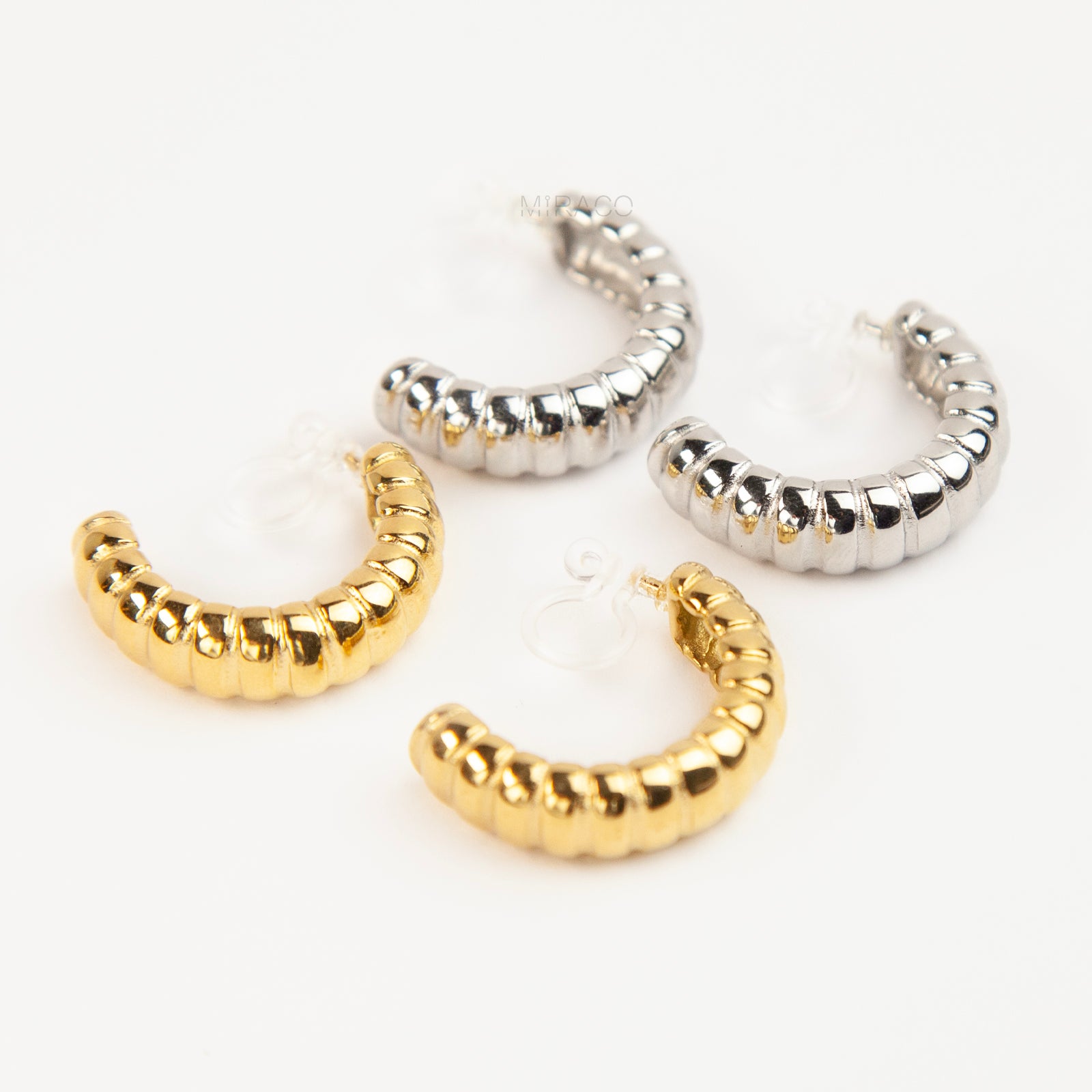 Two pairs of textured croissant-style C-hoop earrings, one pair in gold and one pair in silver, featuring clear invisible resin clip-on backs