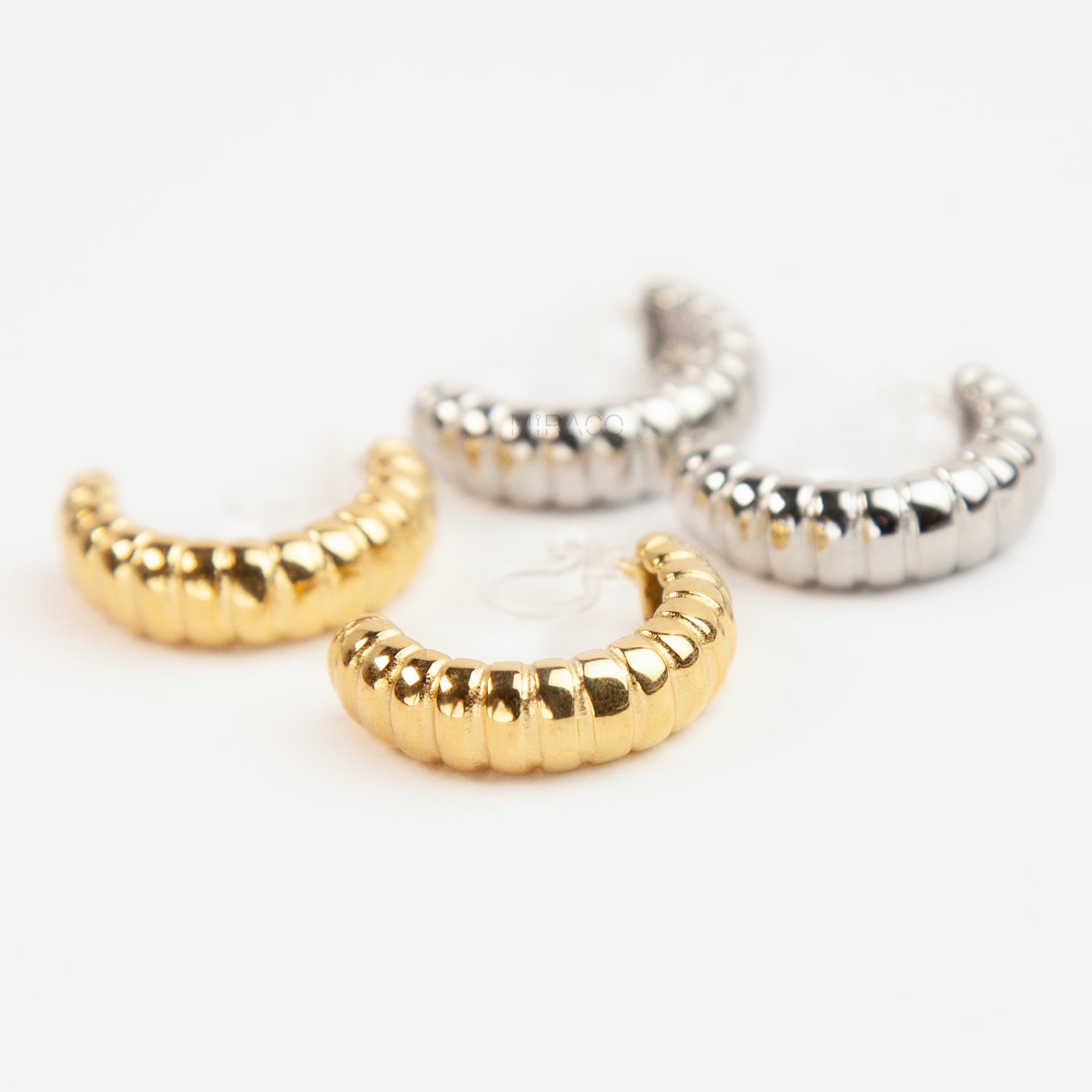 Two pairs of textured croissant-style C-hoop earrings, one pair in gold and one pair in silver, featuring clear invisible resin clip-on backs