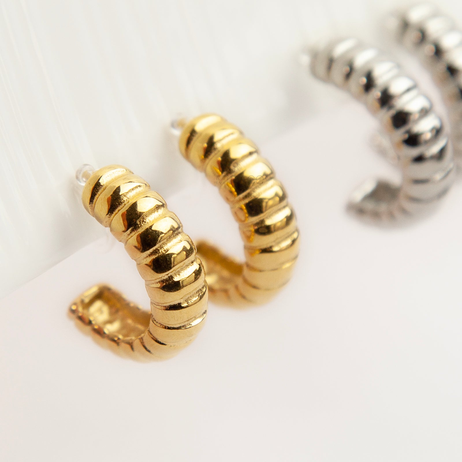 Two pairs of textured croissant-style C-hoop earrings, one pair in gold and one pair in silver, featuring clear invisible resin clip-on backs