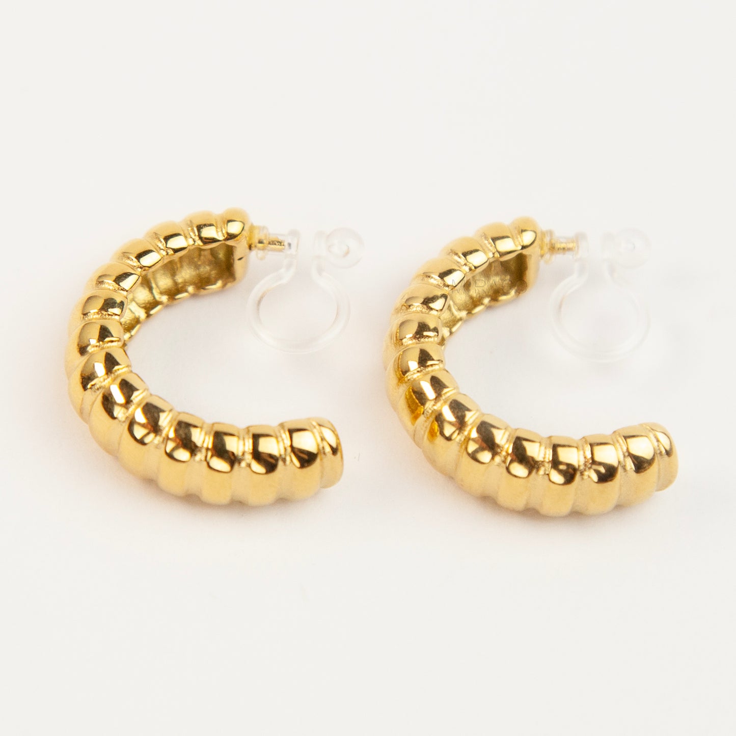 Two pairs of textured croissant-style C-hoop earrings, one pair in gold and one pair in silver, featuring clear invisible resin clip-on backs