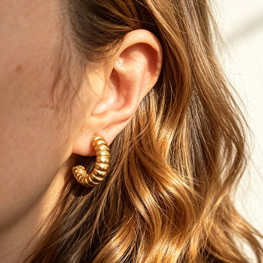 Two pairs of textured croissant-style C-hoop earrings, one pair in gold and one pair in silver, featuring clear invisible resin clip-on backs