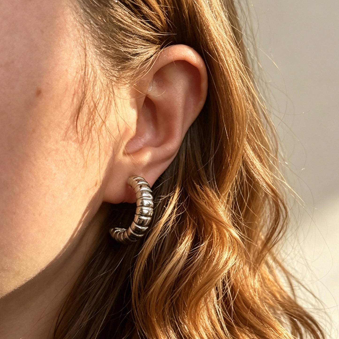 Two pairs of textured croissant-style C-hoop earrings, one pair in gold and one pair in silver, featuring clear invisible resin clip-on backs