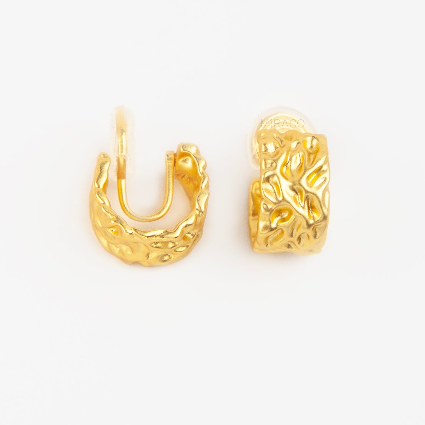 A pair of wide, matte gold-tone clip-on hoop earrings with an organic hammered molten texture, featuring gold adjustable coil-spring backs
