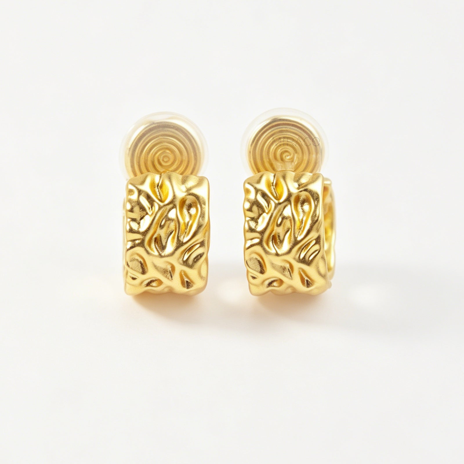 A pair of wide, matte gold-tone clip-on hoop earrings with an organic hammered molten texture, featuring gold adjustable coil-spring backs