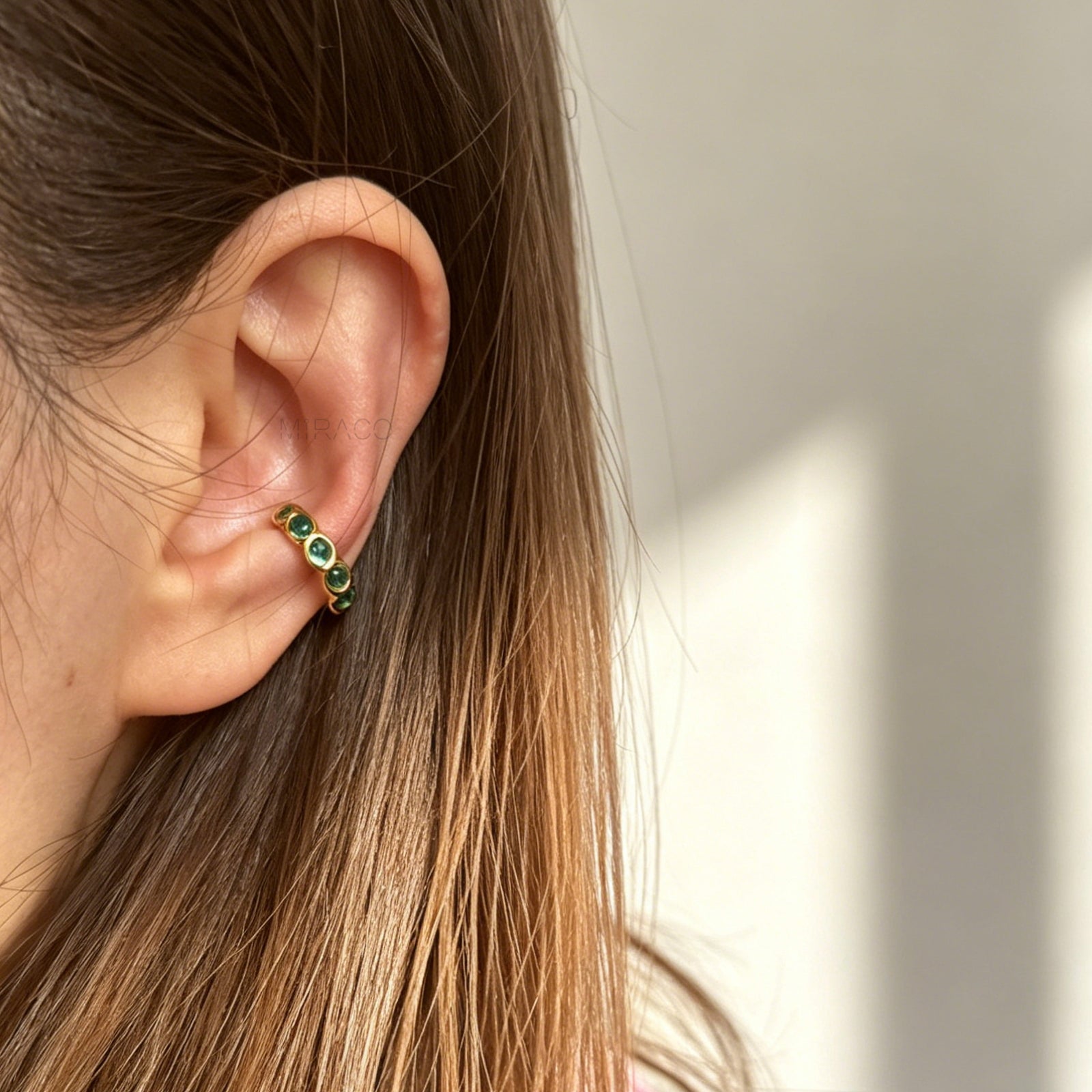 single eternity ear cuffs with bezel-set stones, gold with emerald green crystals.
