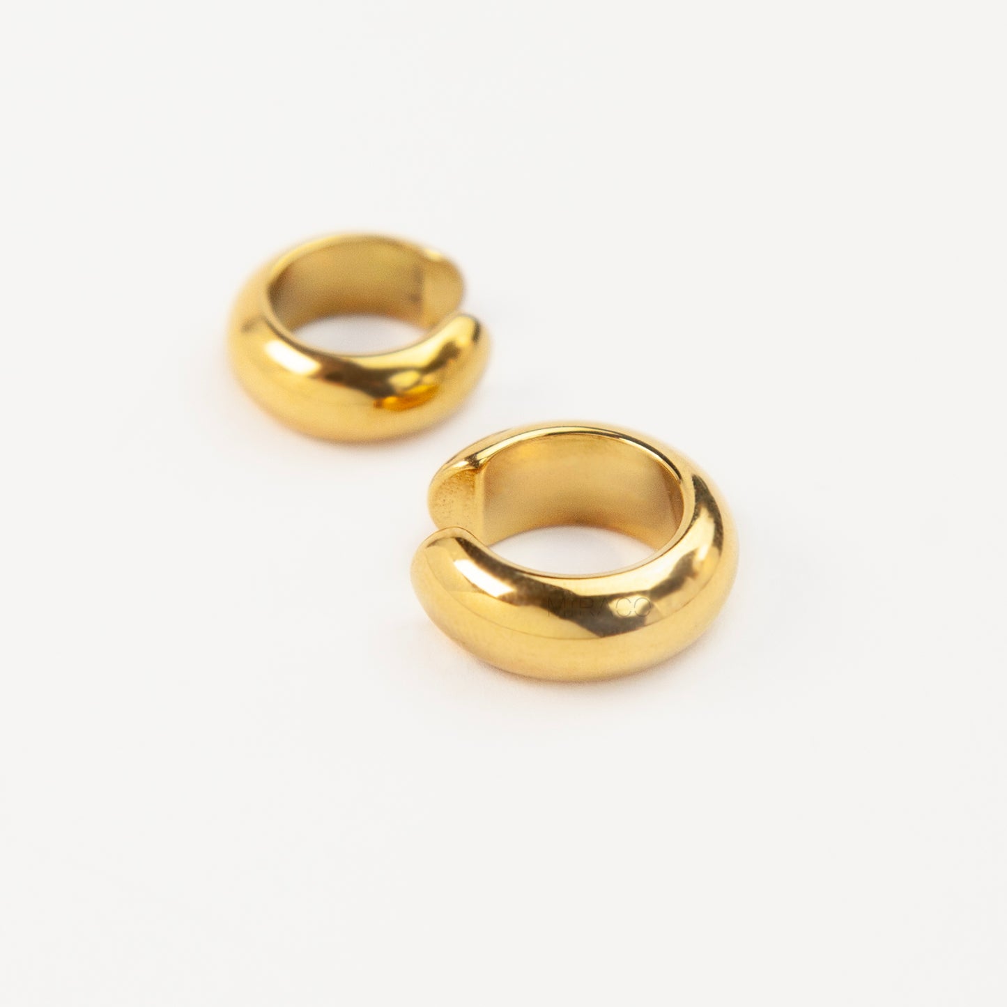 Two chunky, polished gold-tone stainless steel ear cuffs with a smooth, rounded dome design, displayed side-by-side in different sizes on a white background.