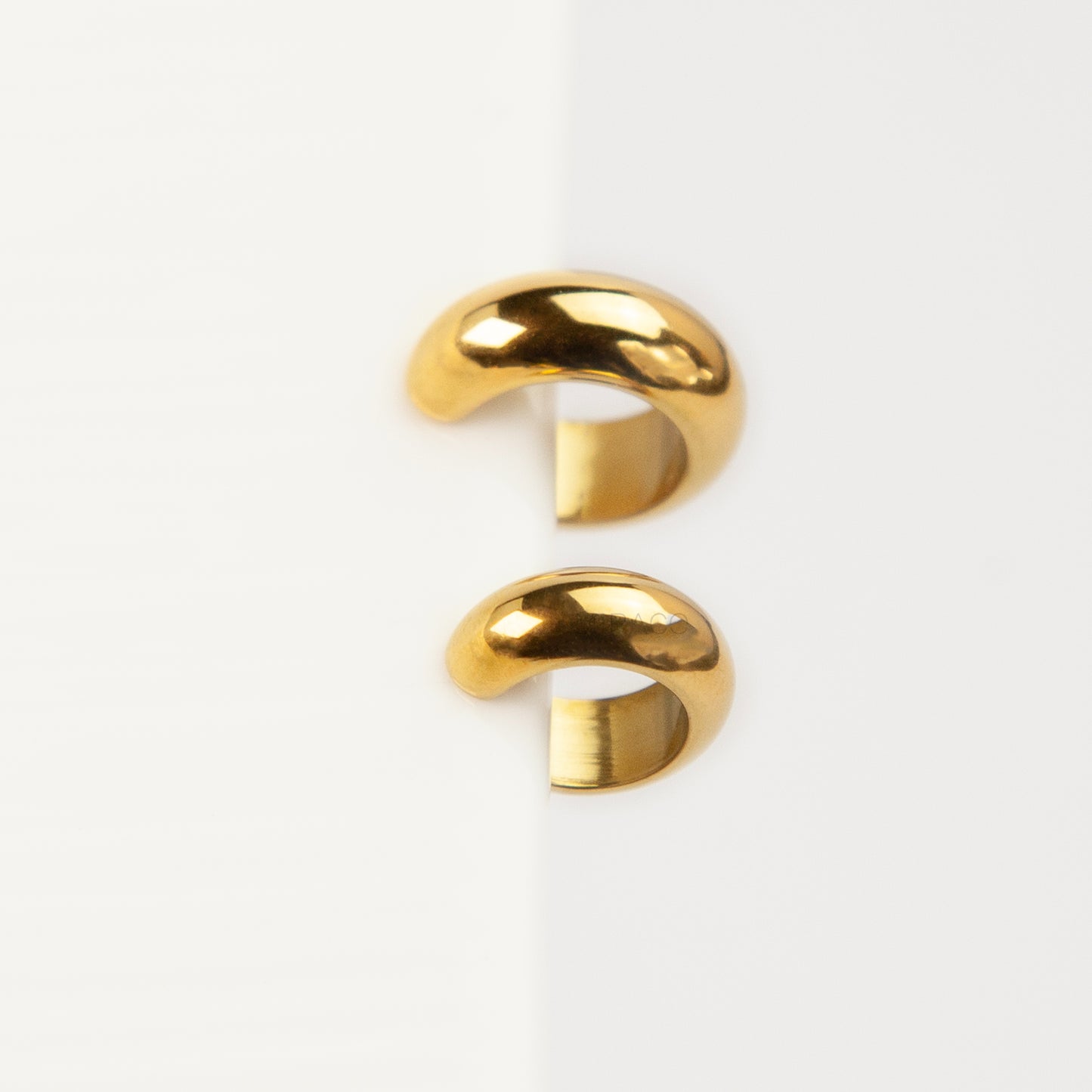 Two chunky, polished gold-tone stainless steel ear cuffs with a smooth, rounded dome design, displayed side-by-side in different sizes on a white background.