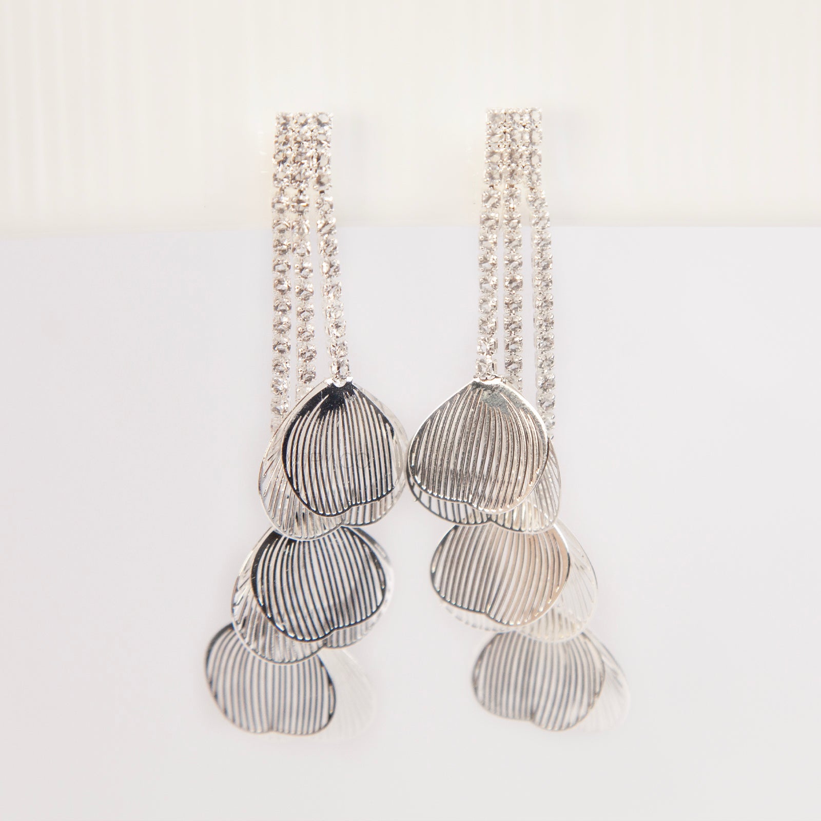 A pair of elegant silver dangle clip-on earrings from clip-on-earrings-clip475-1.jpg, featuring three rows of sparkling rhinestones cascading into textured, hollow metallic leaf elements hanging in tiers.