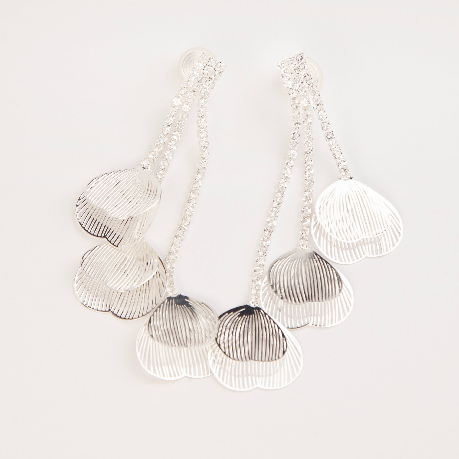 A pair of elegant silver dangle clip-on earrings, featuring three rows of sparkling rhinestones cascading into textured, hollow metallic leaf elements hanging in tiers.