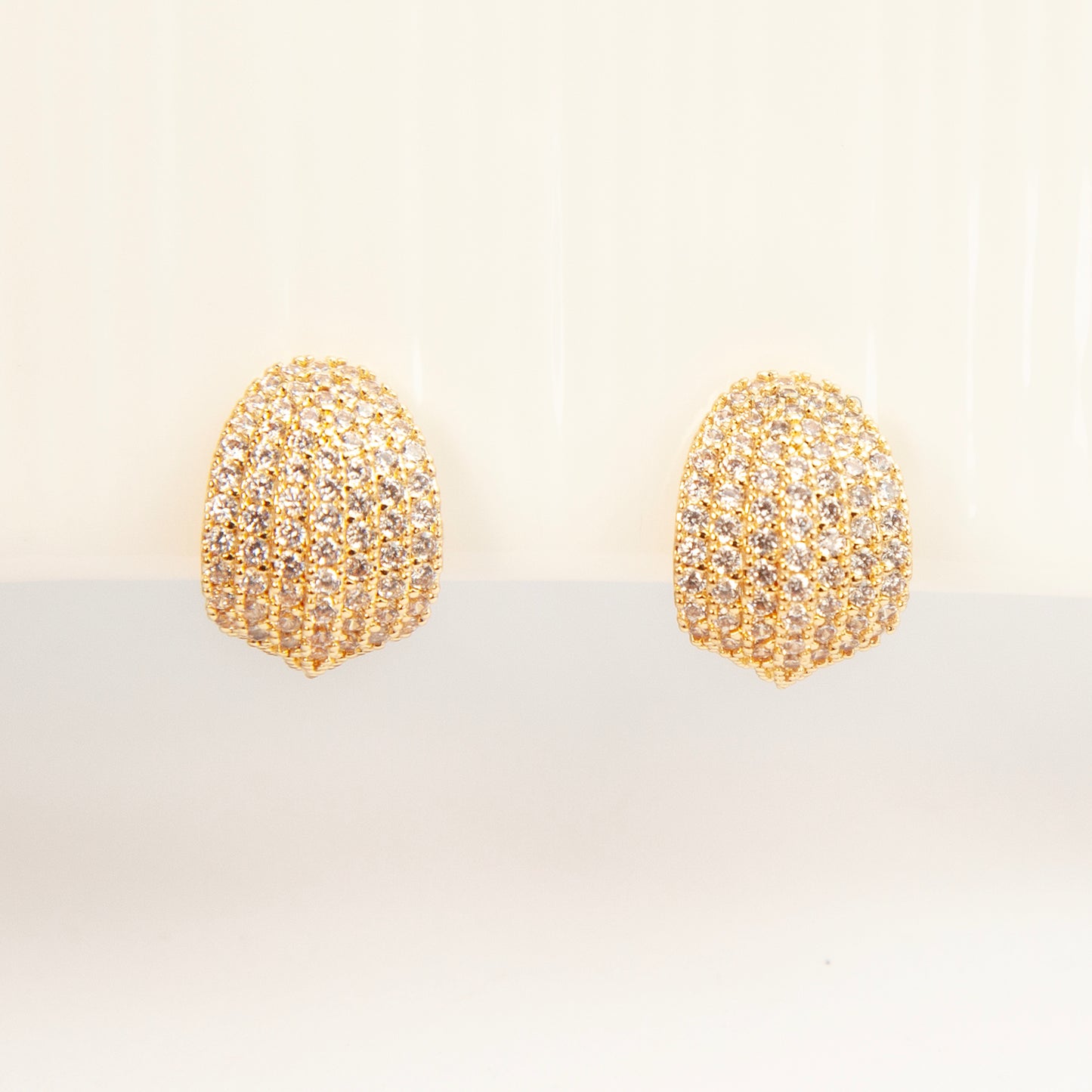A pair of luxurious gold-plated dome clip-on earrings, heavily encrusted with rows of sparkling pave cubic zirconia crystals, featuring comfortable, adjustable spiral coil backs for non-pierced ears.