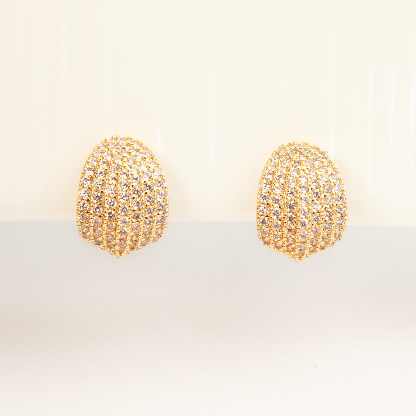 A pair of luxurious gold-plated dome clip-on earrings, heavily encrusted with rows of sparkling pave cubic zirconia crystals, featuring comfortable, adjustable spiral coil backs for non-pierced ears.