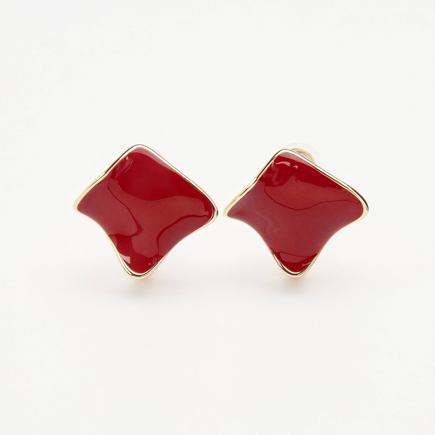A pair of vintage-style gold clip-on earrings, showcasing a distinct wavy rhombus shape filled with smooth, glossy red enamel, fitted with comfortable, invisible-style adjustable coil backs for unpierced ears.