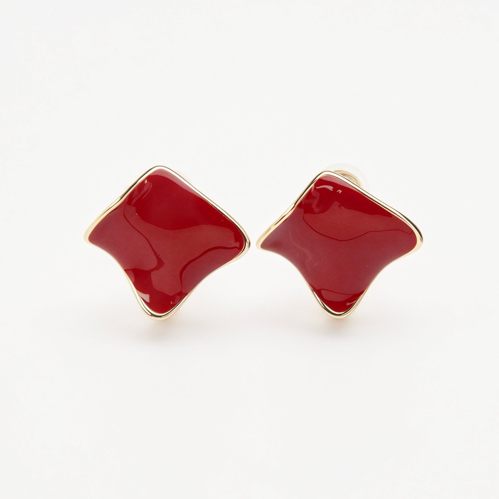 A pair of vintage-style gold clip-on earrings, showcasing a distinct wavy rhombus shape filled with smooth, glossy red enamel, fitted with comfortable, invisible-style adjustable coil backs for unpierced ears.