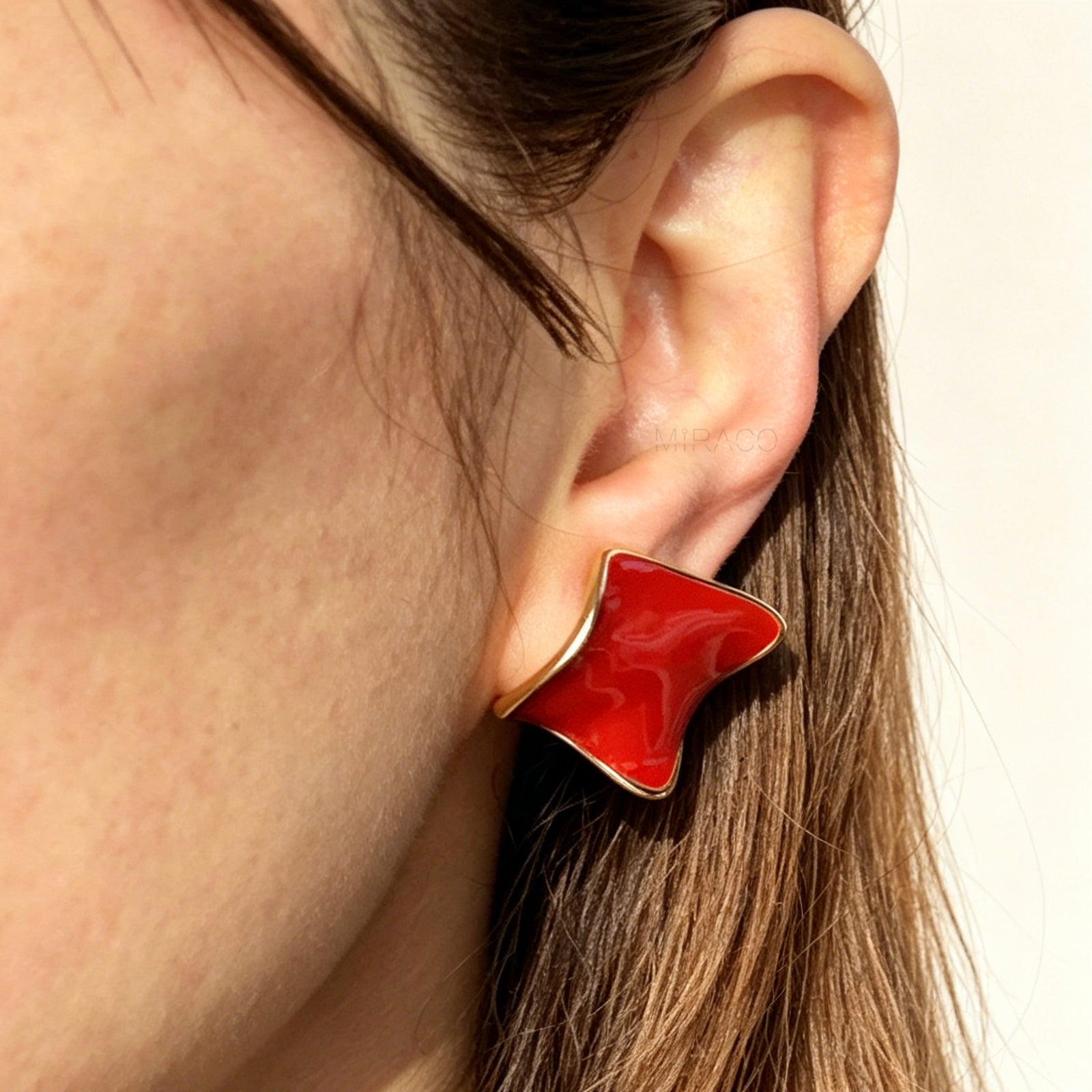 A pair of vintage-style gold clip-on earrings, showcasing a distinct wavy rhombus shape filled with smooth, glossy red enamel, fitted with comfortable, invisible-style adjustable coil backs for unpierced ears.
