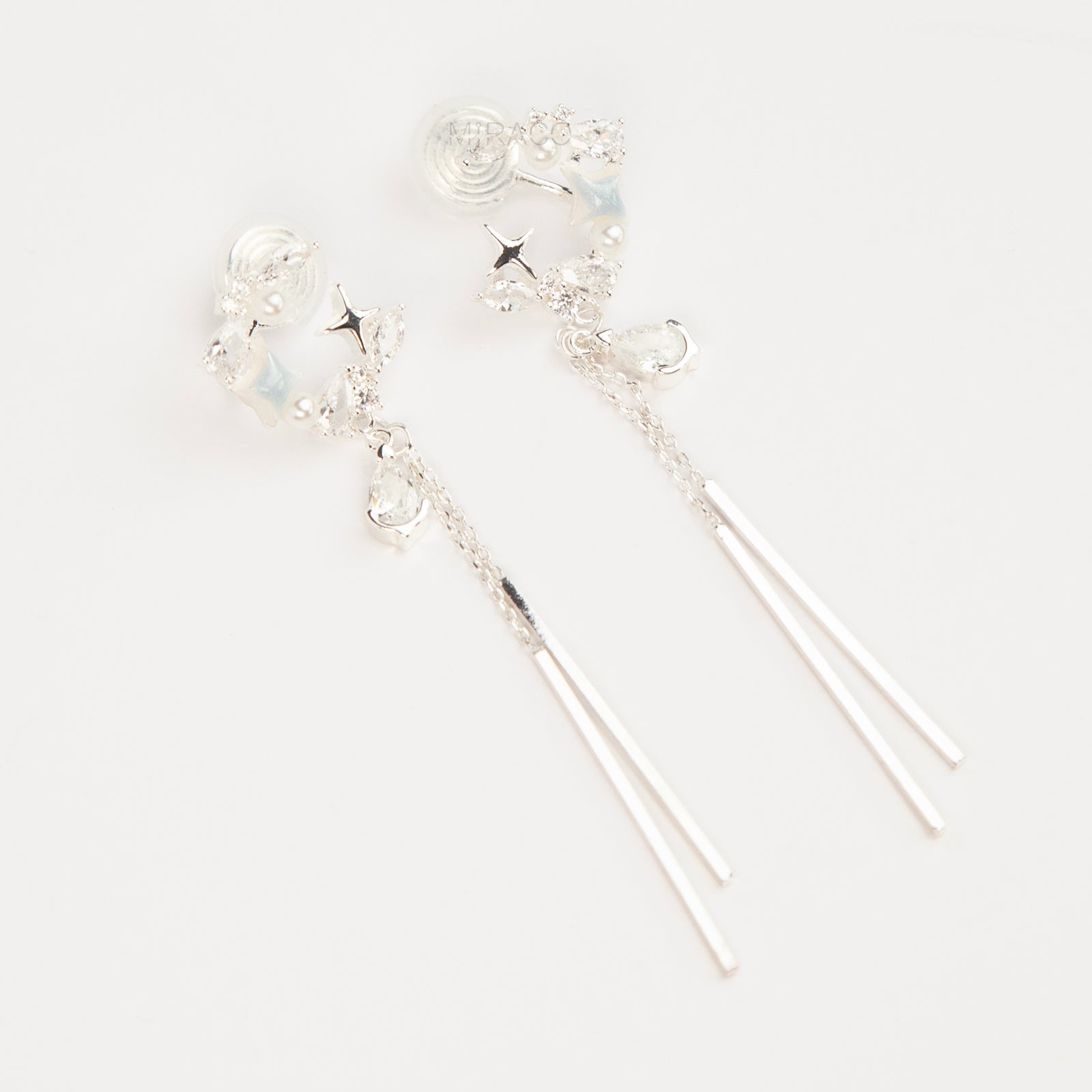A pair of elegant silver celestial dangle clip-on earrings, featuring a crescent moon and star design accented with marquise crystals and tiny pearls, cascading into a teardrop gemstone and sleek, vertical metallic bar tassels on comfortable coil backs.