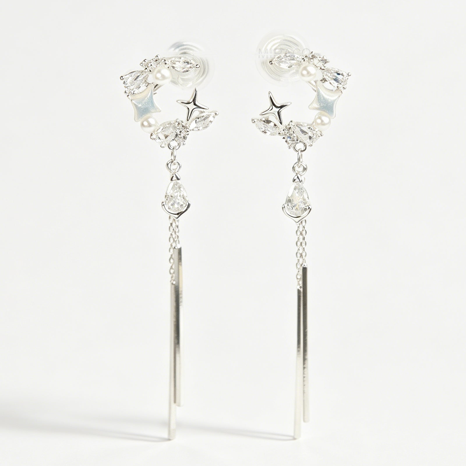 A pair of elegant silver celestial dangle clip-on earrings, featuring a crescent moon and star design accented with marquise crystals and tiny pearls, cascading into a teardrop gemstone and sleek, vertical metallic bar tassels on comfortable coil backs.