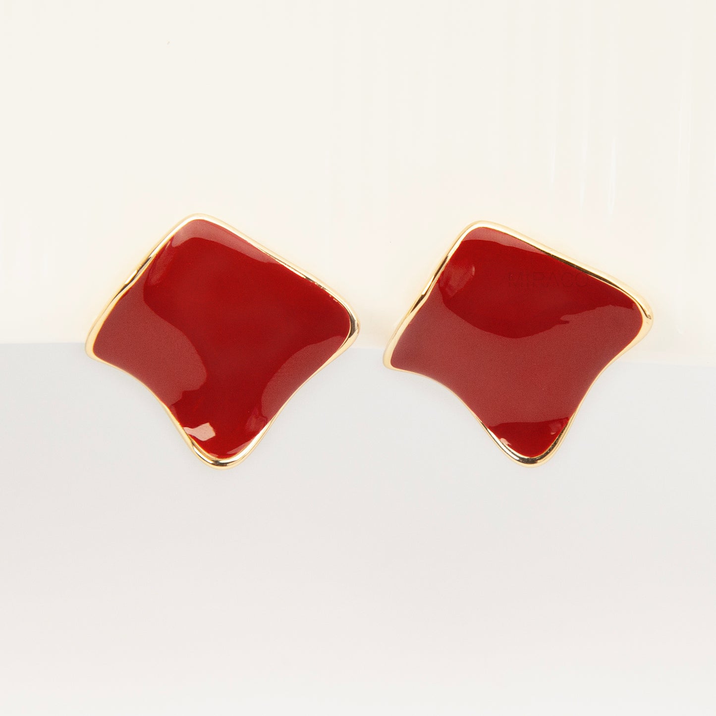 A pair of vintage-style gold clip-on earrings, showcasing a distinct wavy rhombus shape filled with smooth, glossy red enamel, fitted with comfortable, invisible-style adjustable coil backs for unpierced ears.