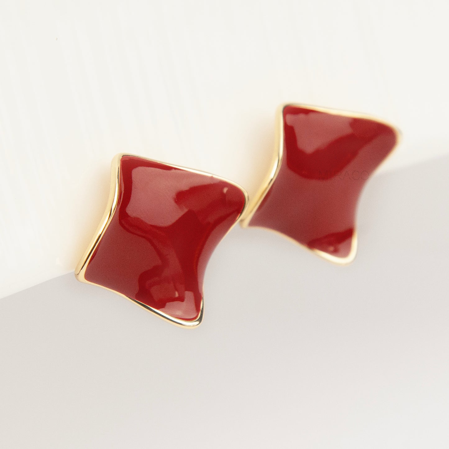 A pair of vintage-style gold clip-on earrings, showcasing a distinct wavy rhombus shape filled with smooth, glossy red enamel, fitted with comfortable, invisible-style adjustable coil backs for unpierced ears.