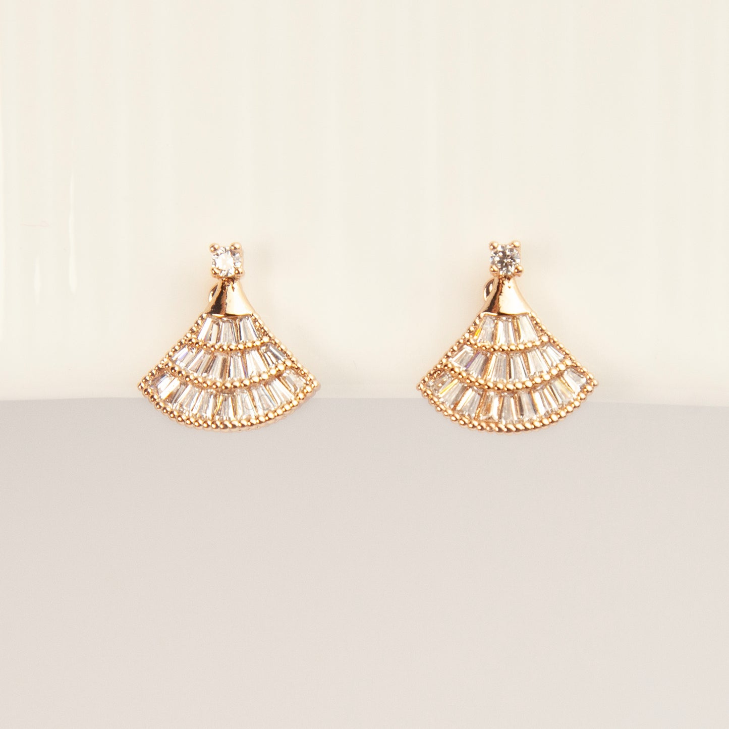 A pair of gold Art Deco fan-shaped clip-on earrings, detailed with tiered baguette crystals and fitted with comfortable coil backs featuring clear comfort cushions.