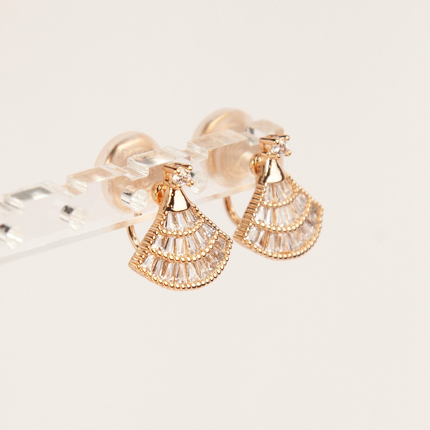 Gold and clear fan-shaped earrings on a light gray background