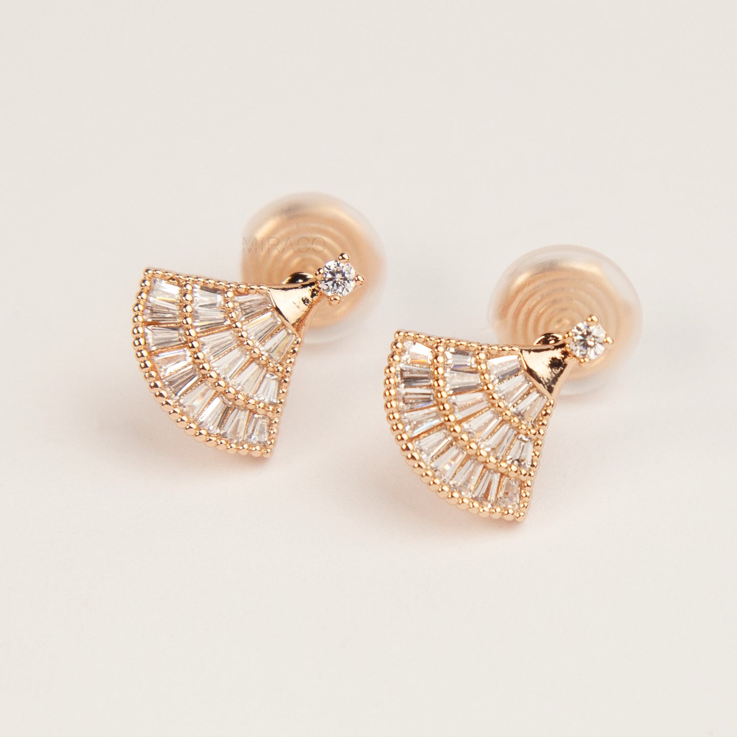 Rose gold fan-shaped earrings with clear gemstones on a light background