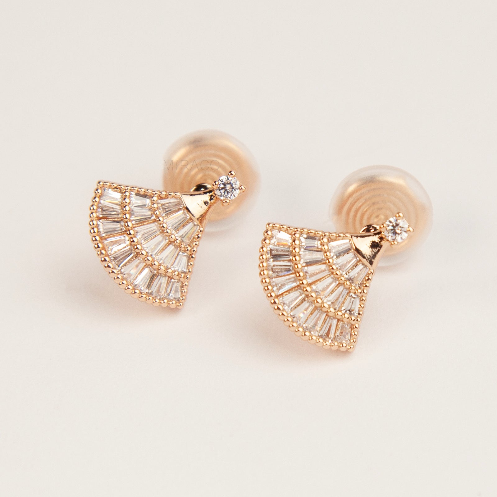 Rose gold fan-shaped earrings with clear gemstones on a light background