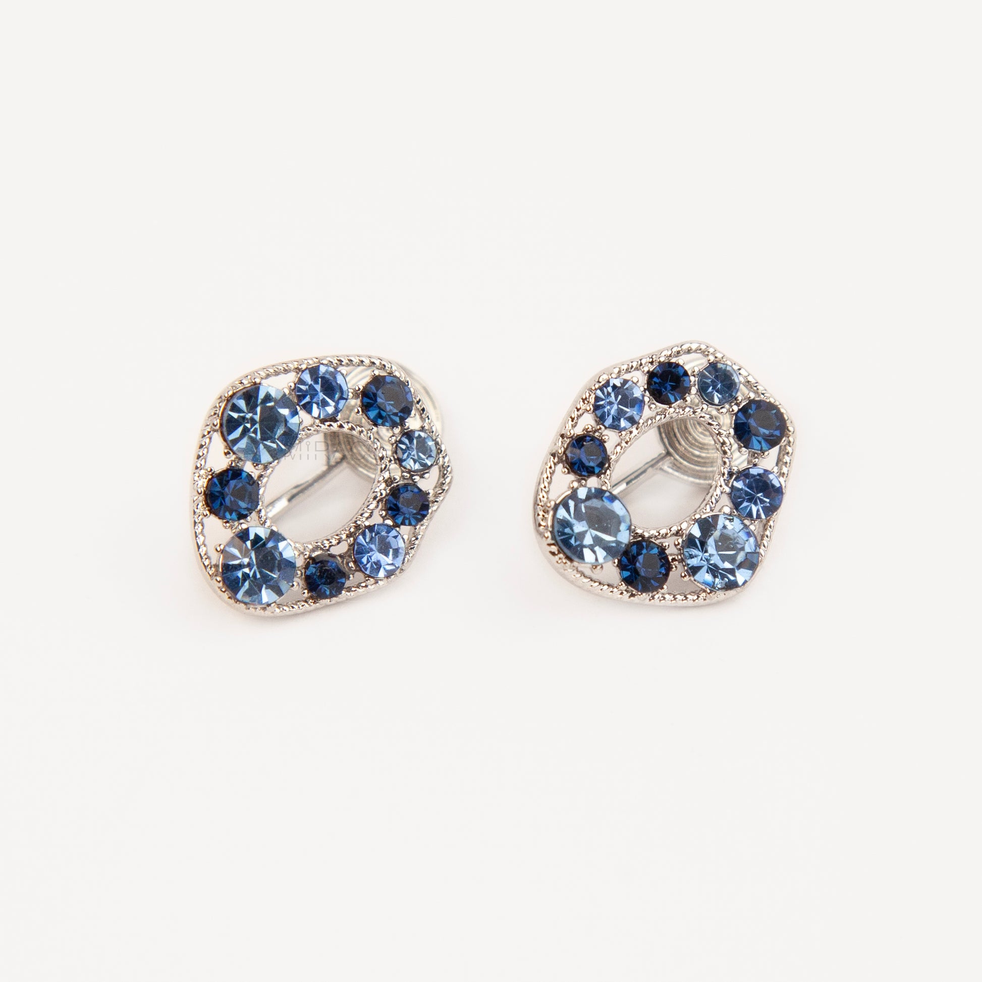 Pair of oval silver-tone non-pierced clip-on earrings with coil backs, set with sparkling dark and light blue crystals.