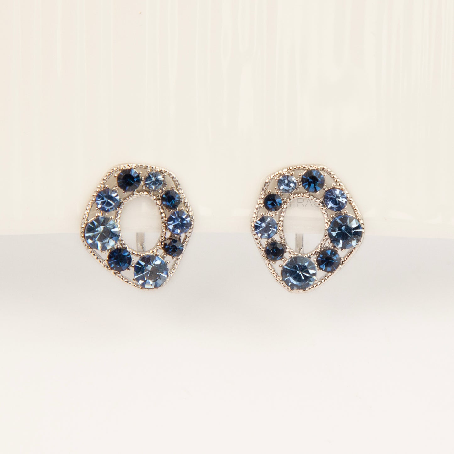 Pair of oval silver-tone non-pierced clip-on earrings with coil backs, set with sparkling dark and light blue crystals.