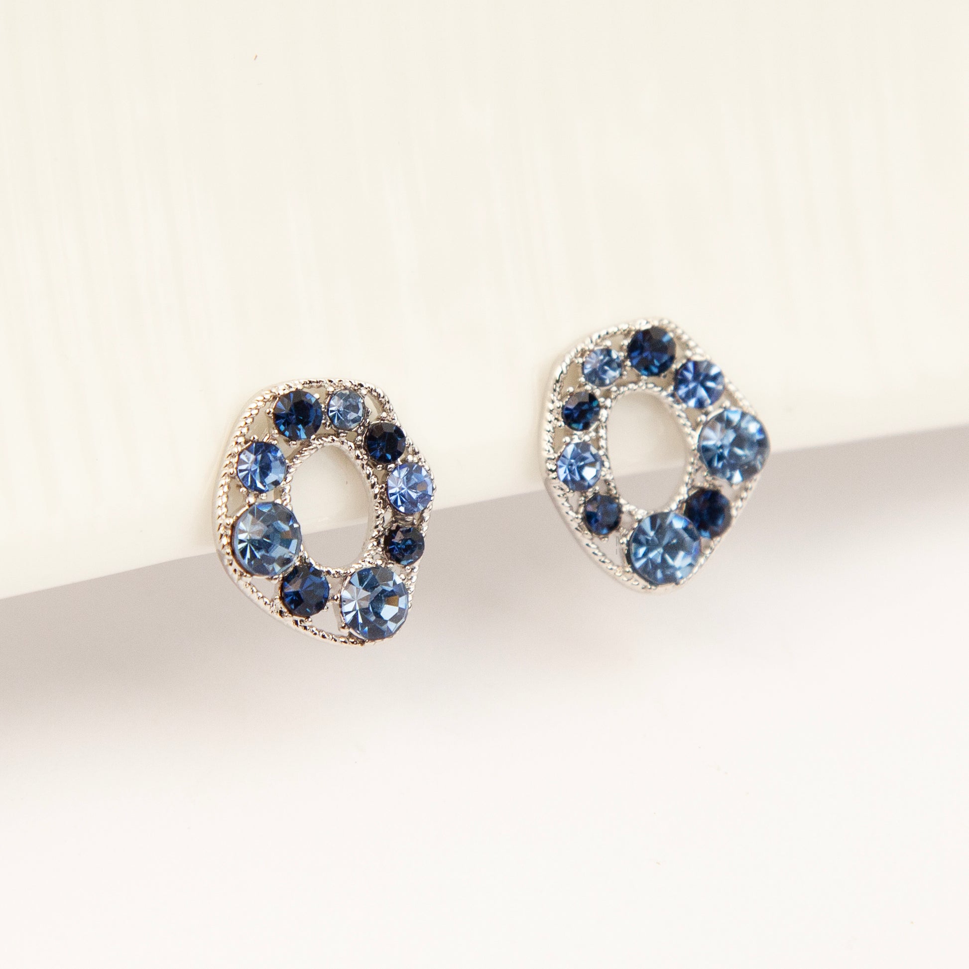 Pair of oval silver-tone non-pierced clip-on earrings with coil backs, set with sparkling dark and light blue crystals.