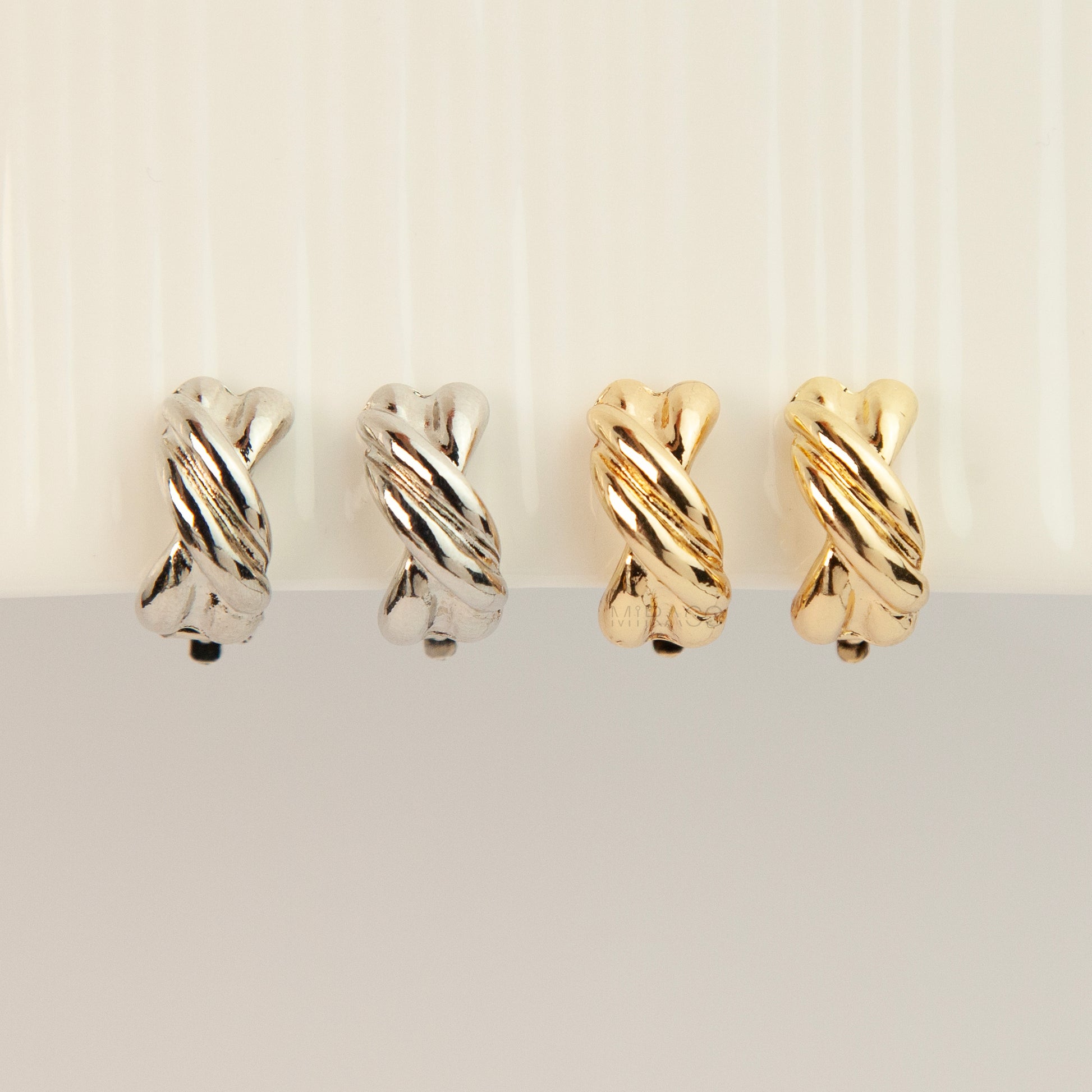 Chunky twisted crossover clip-on hoop earrings with paddle backs displayed in silver and gold tones.