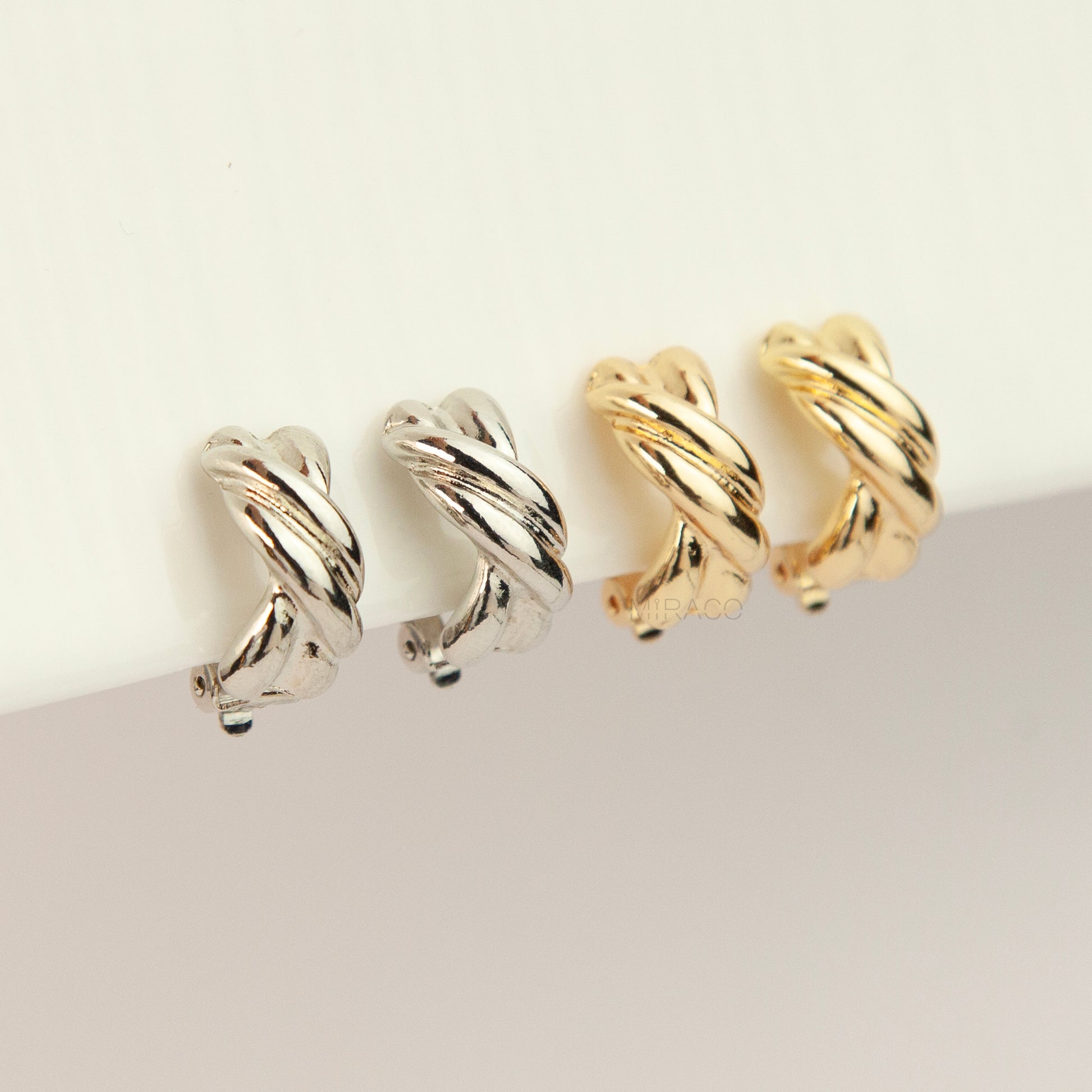 Chunky twisted crossover clip-on hoop earrings with paddle backs displayed in silver and gold tones.