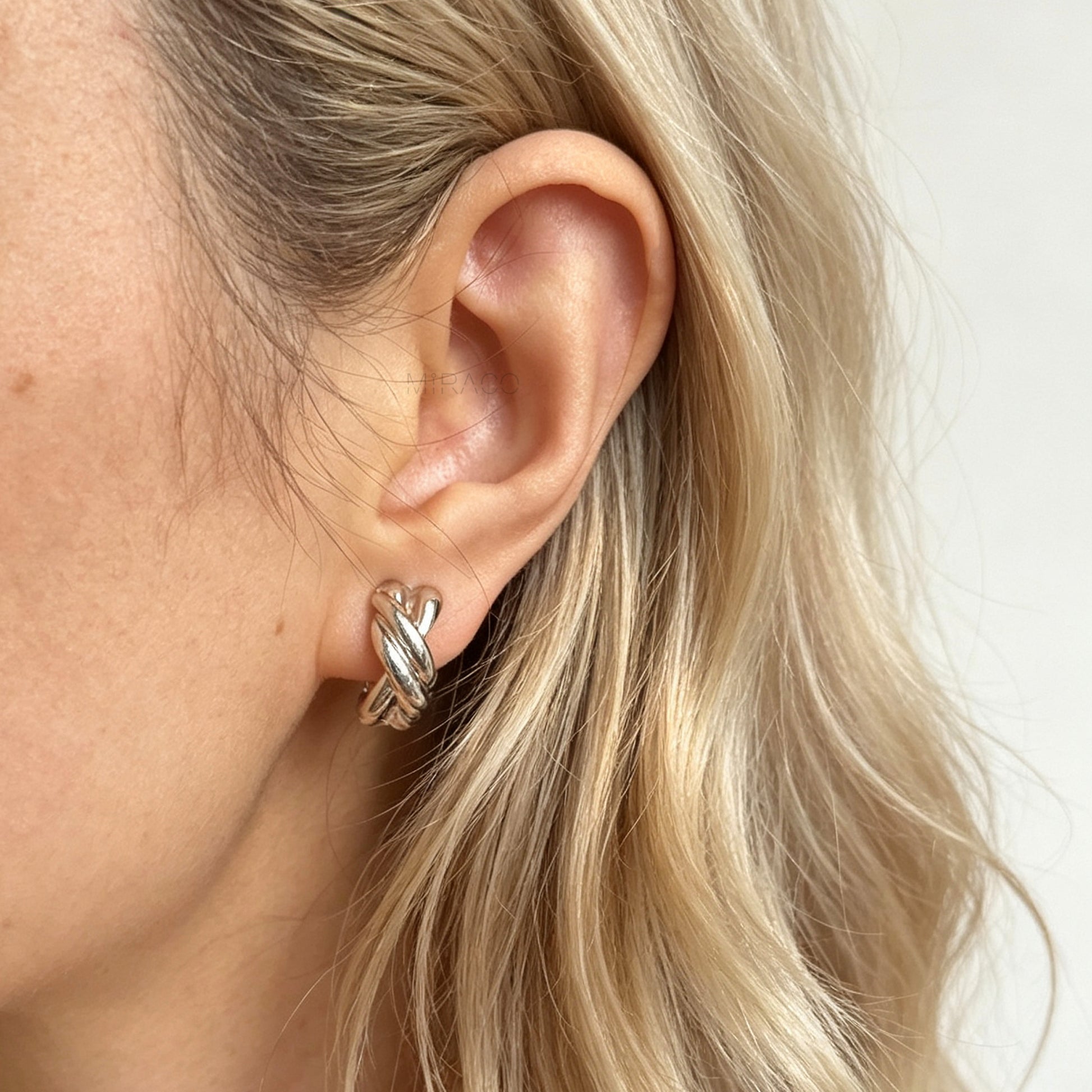 Chunky twisted crossover clip-on hoop earrings with paddle backs displayed in silver and gold tones.