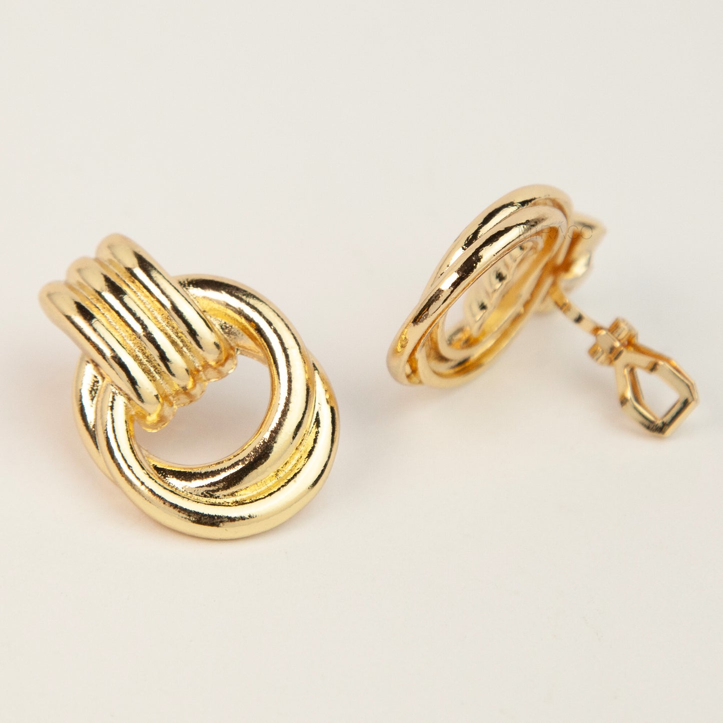Gold and silver non-pierced double ring door knocker clip-on earrings with ribbed texture tops and mini clip backs displayed side by side.
