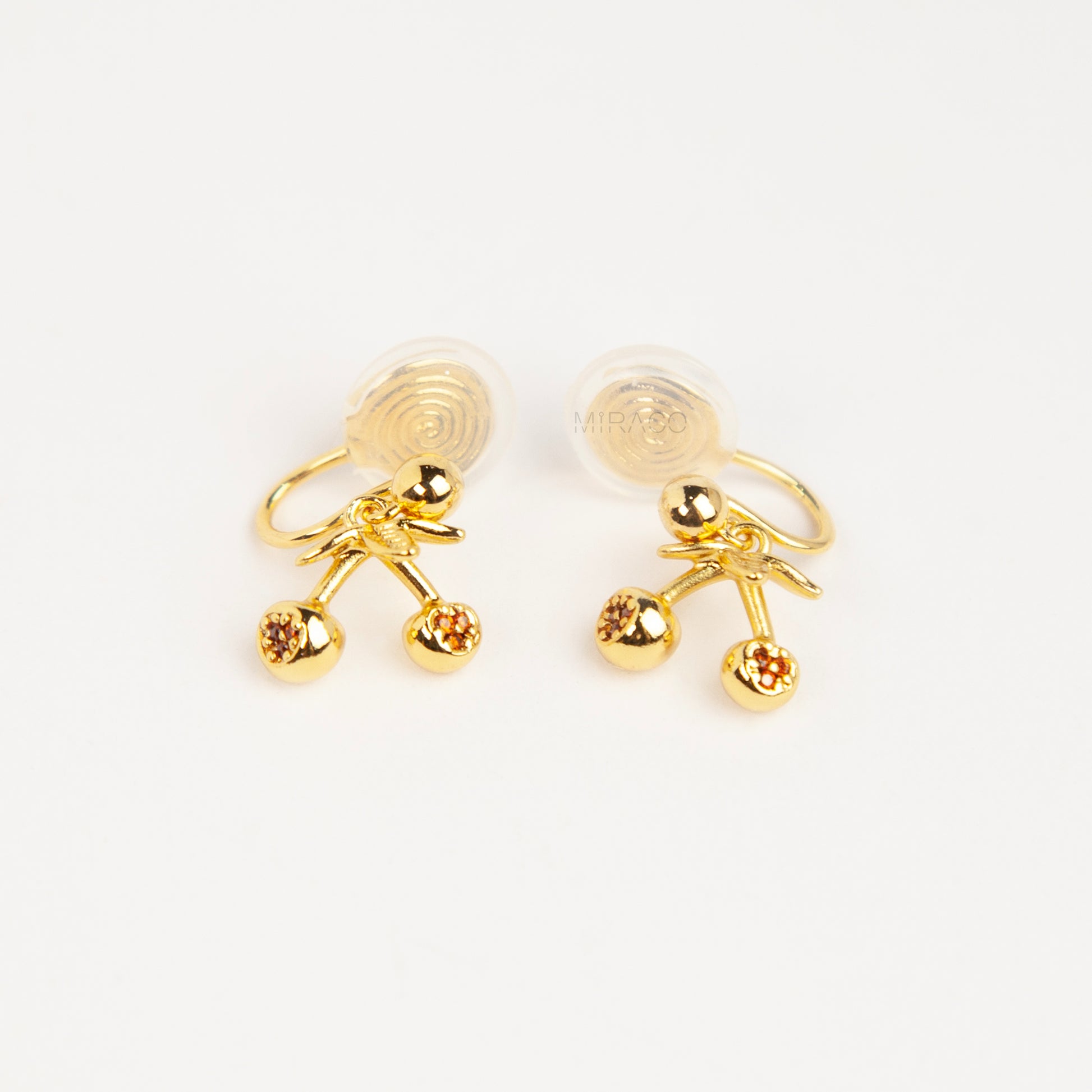 Pair of polished gold-toned double cherry clip-on earrings with amber rhinestone accents and comfortable silicone-backed spiral coil clips.